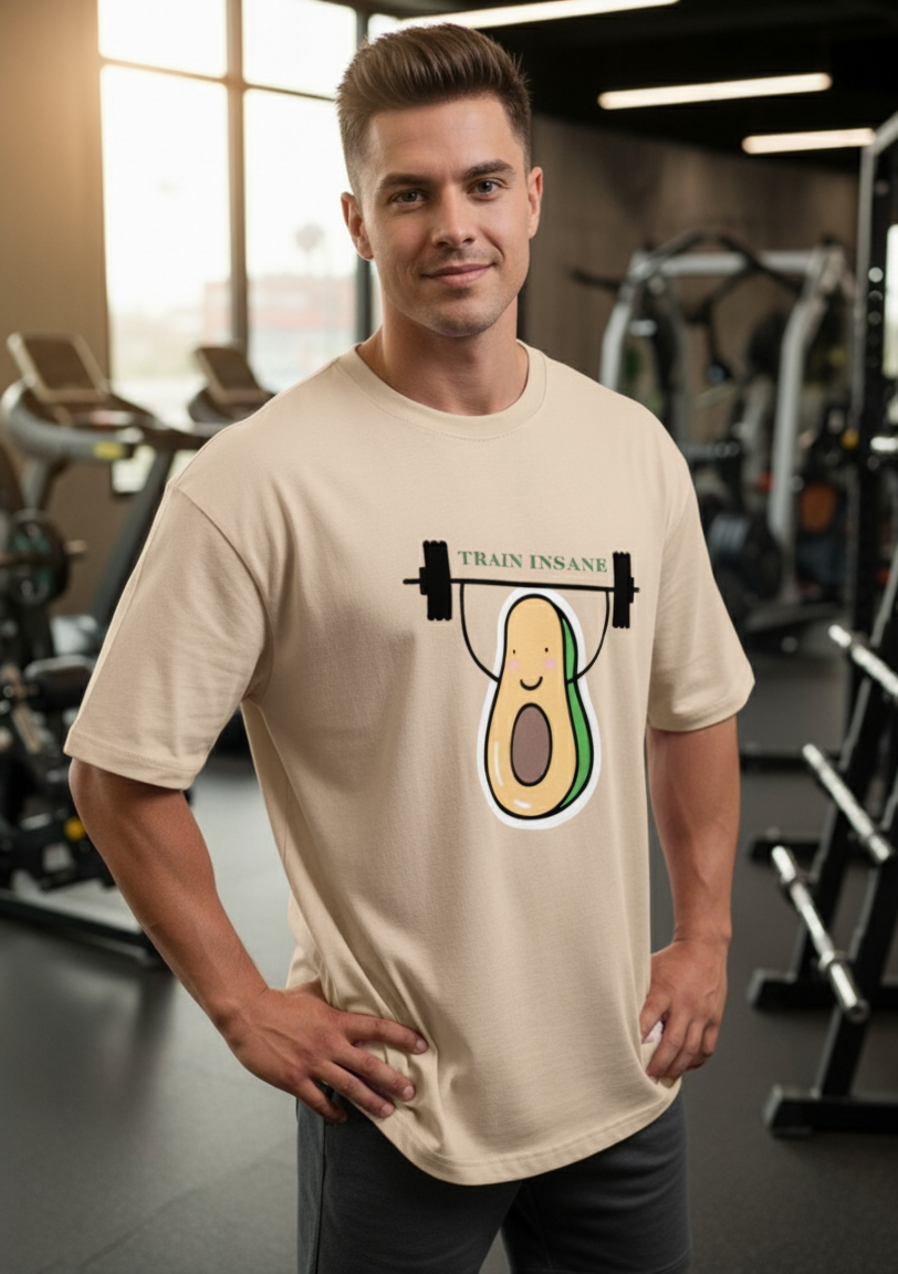 Man wearing a beige t-shirt with an avocado lifting weights graphic in a gym.