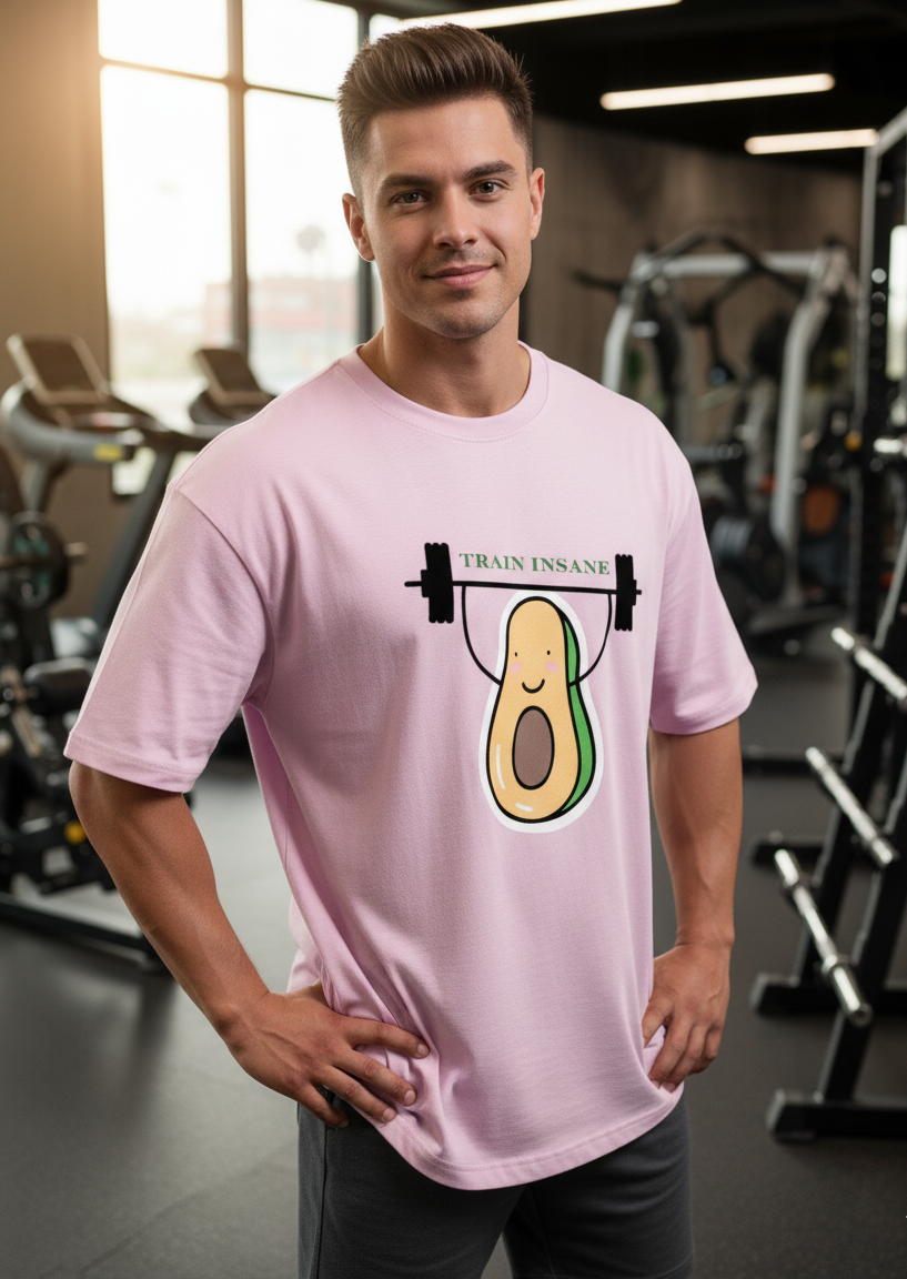 Man wearing a light baby pink t-shirt with an avocado lifting weights graphic in a gym.