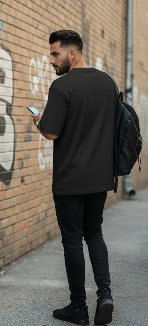 Man in black clothing with a backpack looking at his phone against a graffiti-covered wall.