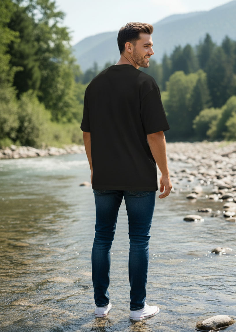 Man wearing black t-shirt walking along a river with mountains and trees in the background
