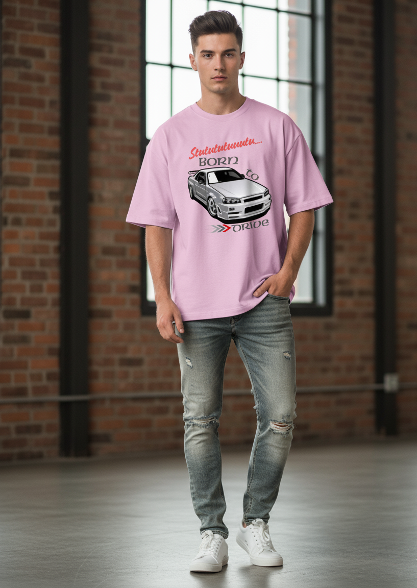 Man wearing a light baby pink t-shirt with a car graphic in a room with brick walls and large windows.
