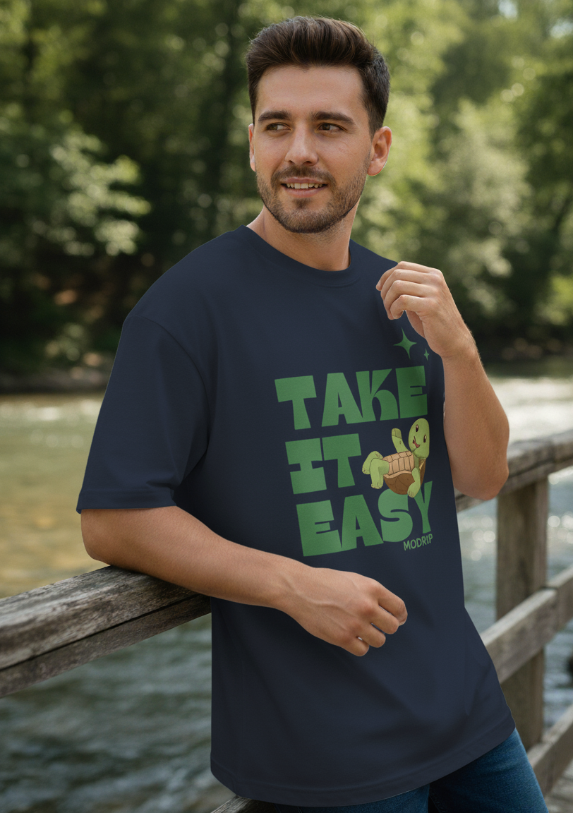 Man wearing a navy blue t-shirt with 'Take It Easy' graphic design outdoors by a body of water.