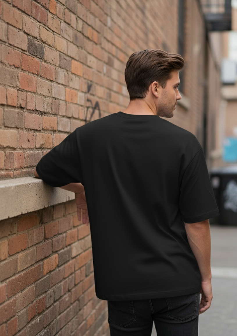 Man wearing a black t-shirt leaning against a brick wall.