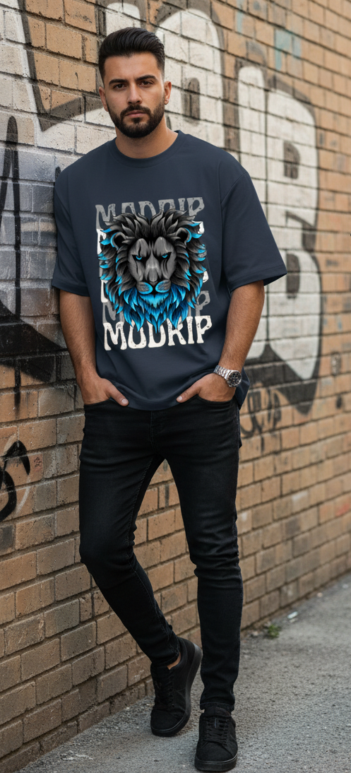 Man wearing a navy blue t-shirt with a graphic design standing against a graffiti-covered wall.