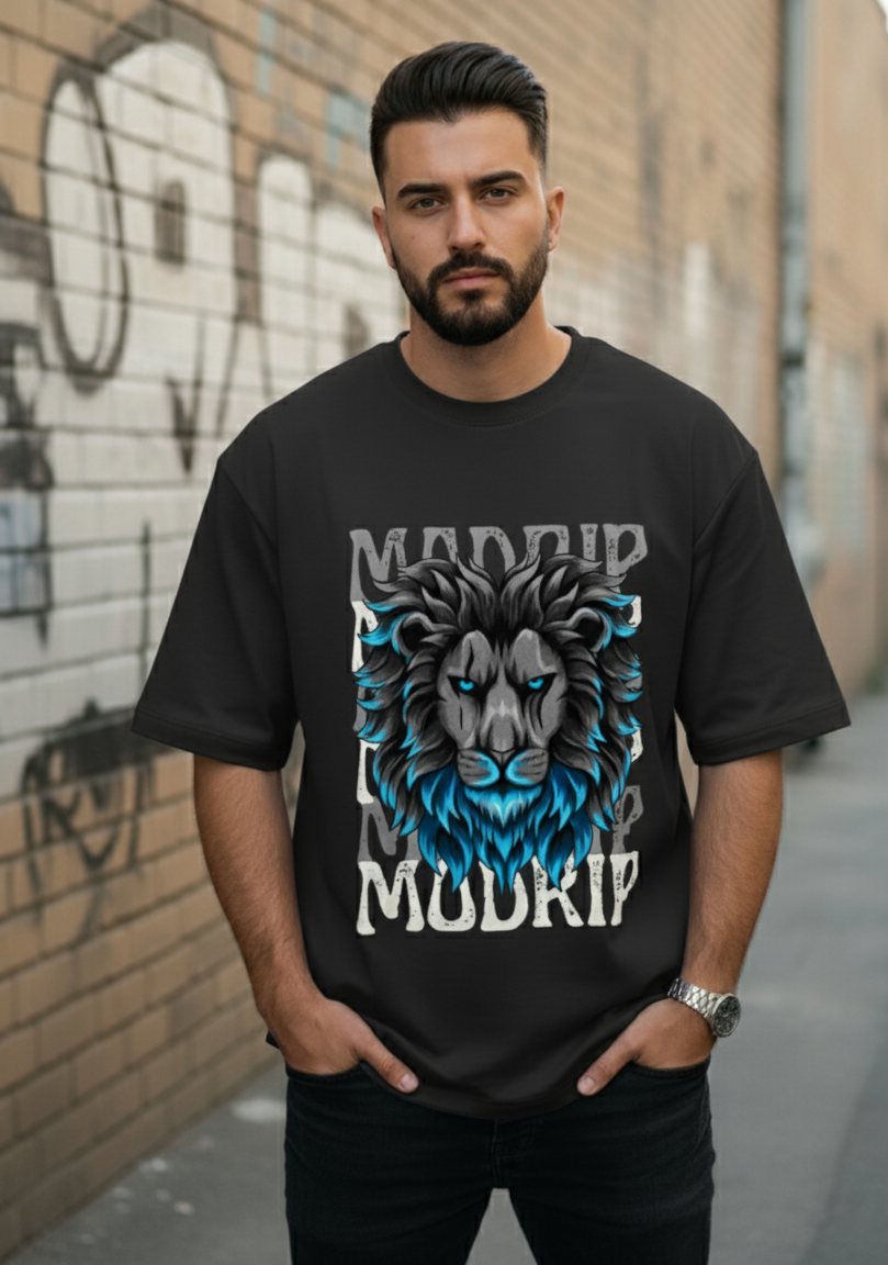 Man wearing a black t-shirt with a graphic design of a lion and text, standing against a graffiti-covered wall.