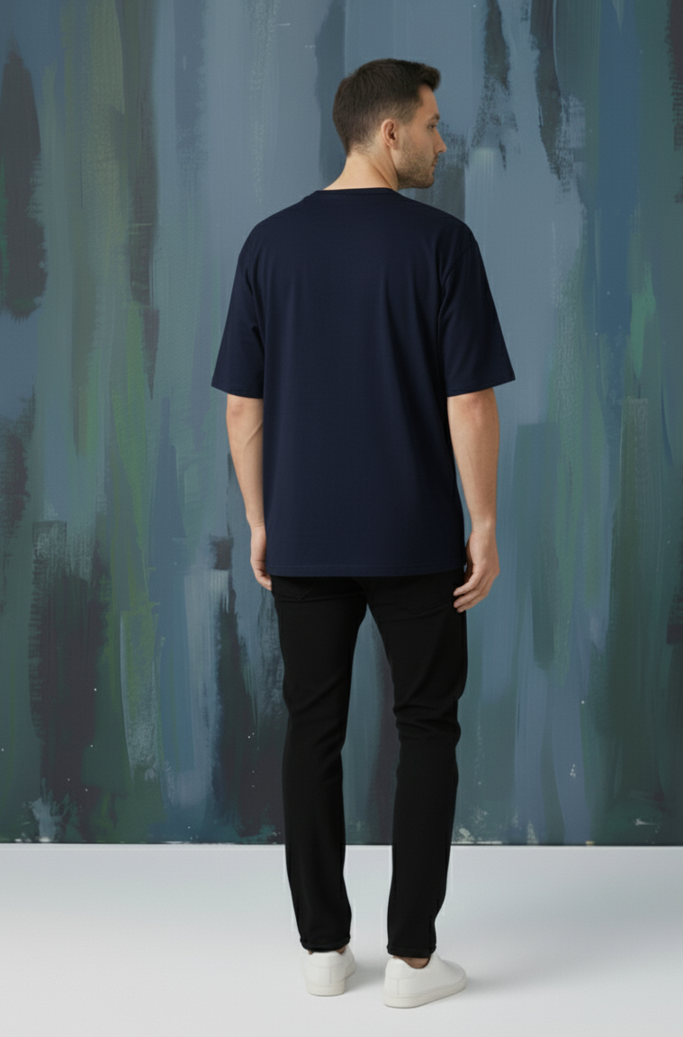 Man wearing a navy blue t-shirt standing against an abstract wall.