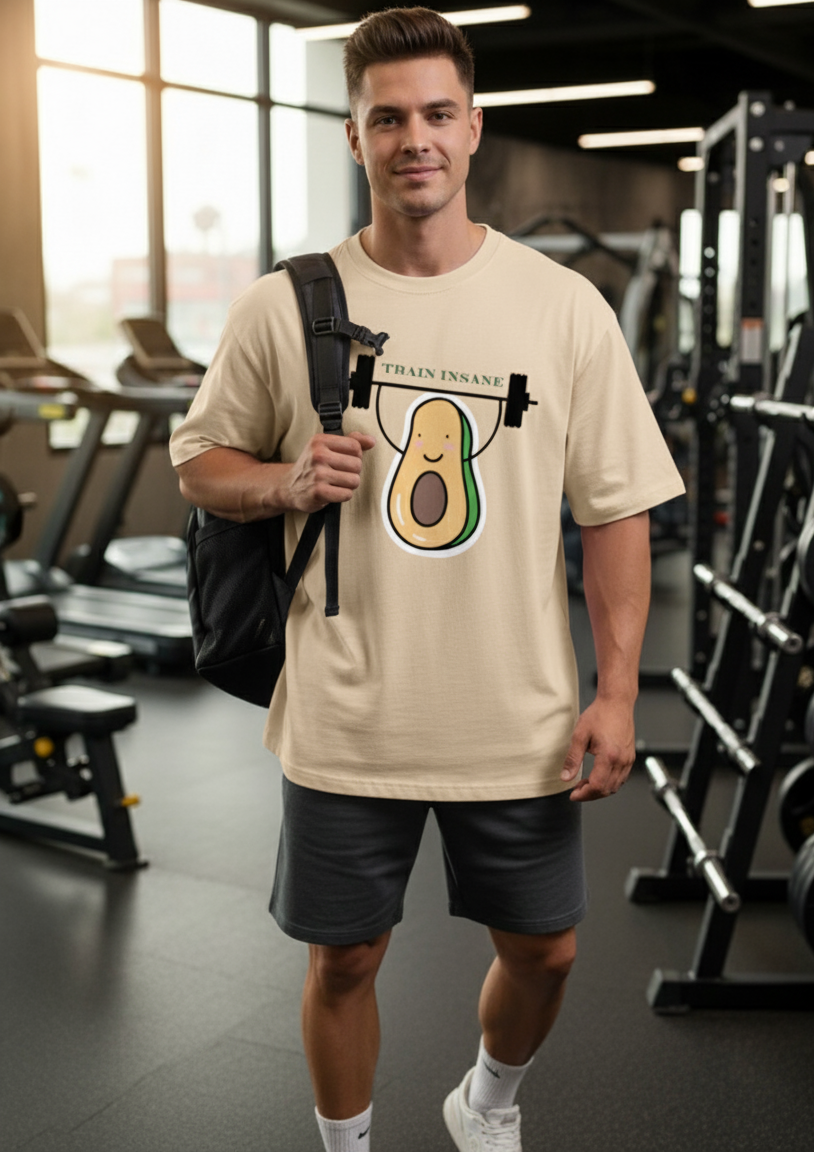 Man in a gym wearing a beige t-shirt with an avocado graphic and 'Train Insane' text.