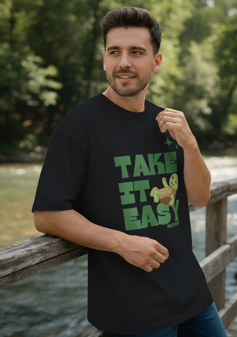 Man wearing a black t-shirt with text and graphic, standing outdoors by a body of water.